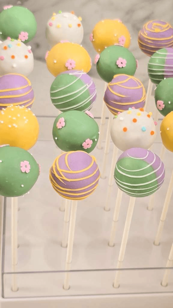 Pastel-coated cake pops with sprinkles and sugar flowers on a white stand